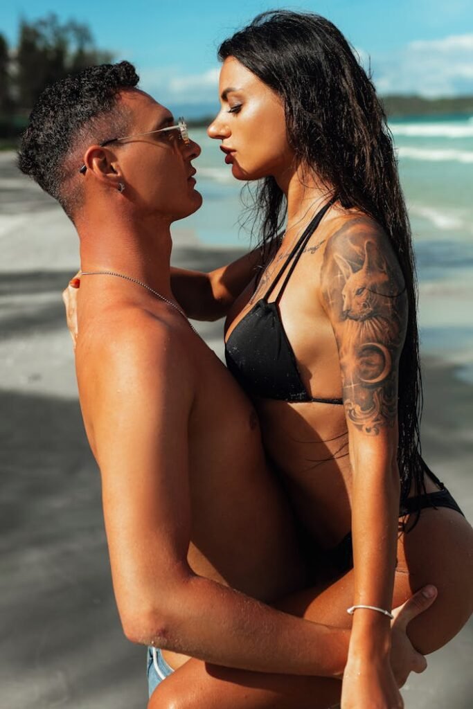 A couple in swimwear share an intimate moment on a sunny beach, exuding romance and summer vibes.